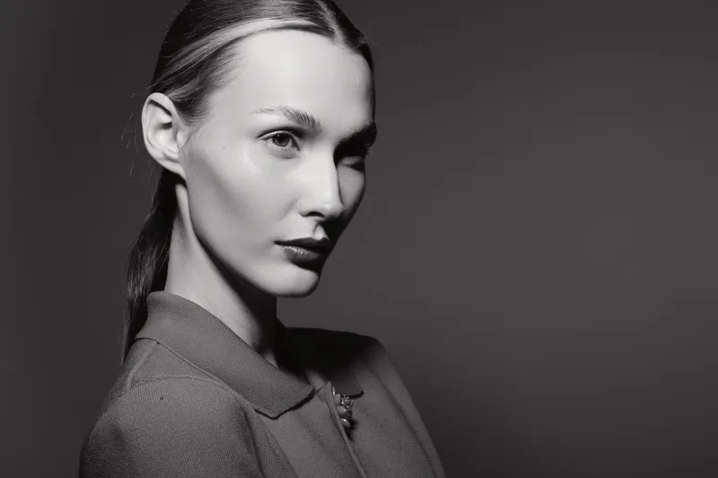Portrait of a caucasian woman with fair skin and slicked back hair wears a grey top against dark background. Concept of elegance, fashion, and beauty in studio lighting.