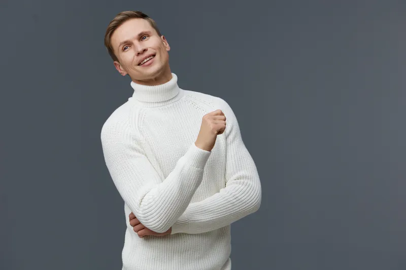 smiling man wearing white knit sweater looking up thoughtful isolated on grey background casual pose mental health gadgets concept