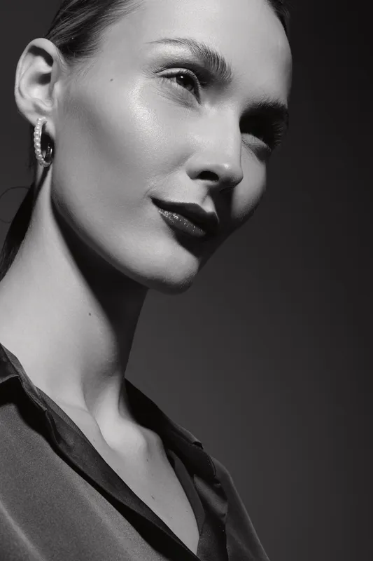 Close-up portrait of a young Caucasian woman with fair skin looking confident. Studio lighting highlights her facial features and smooth skin texture.