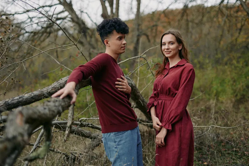 A candid outdoor portrait of a young couple by a fallen tree, capturing natural poses and subtle emotion that emphasize authenticity and credibility in their relaxed, genuine connection.