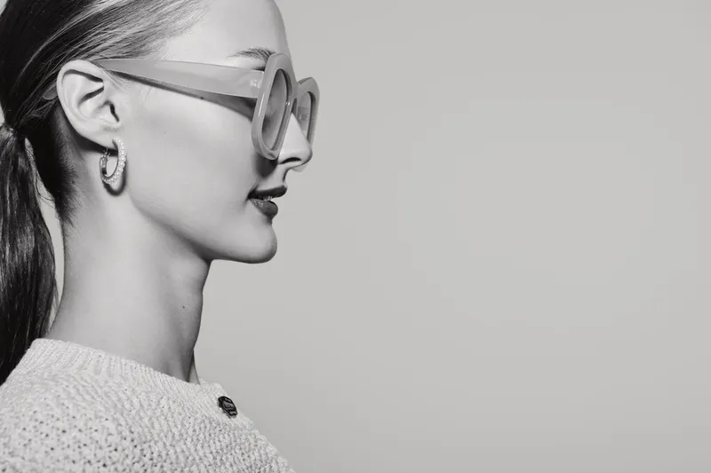 Profile of a white woman with pale skin wearing stylish glasses and earrings against a plain background. Concept of fashion and minimalism.