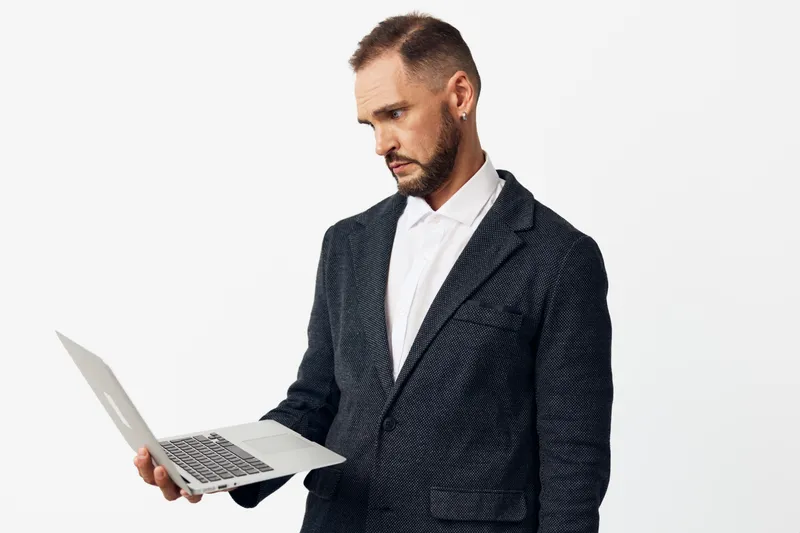 A business professional man stands with a laptop, focused and confident, set against an isolated colored background, conveying determination and calm emotion in a modern work scene.