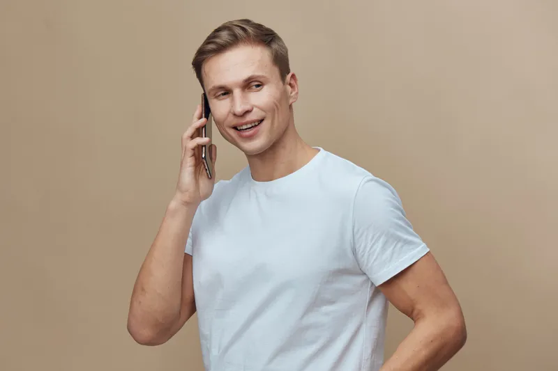 Smiling young caucasian man talking phone casual wear standing beige background digital nomad lifestyle communication concept