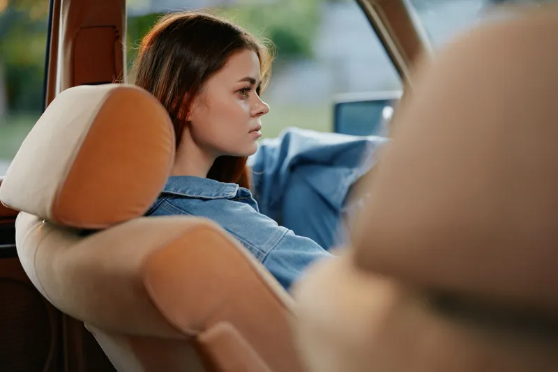 Thoughtful young woman driving an old car, wearing a denim jacket, showcasing emotions of contemplation in a serene outdoor setting.