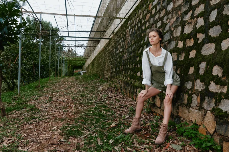 Young woman in a green outfit poses confidently against a rustic stone wall, showcasing fall foliage and earthy tones, ideal for fashion, nature, and seasonal themes