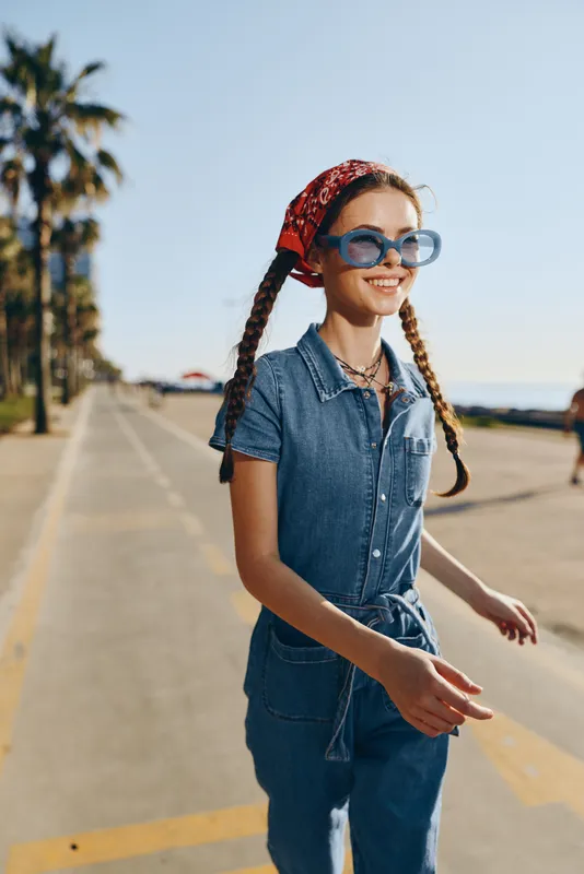 Lifestyle woman in modern boho-western denim street style wearing sunglasses and a red bandana, enjoying a sunny day with a film color effect enhancing the vibrant mood.
