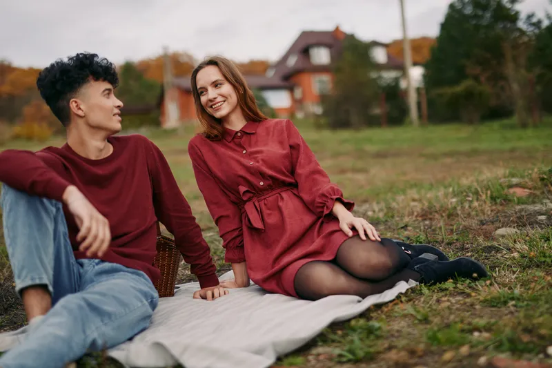 Warm candid portrait of a young couple sitting on a blanket in a suburban park, relaxed and smiling, showing authenticity and credibility through natural gestures, eye contact and warmth.