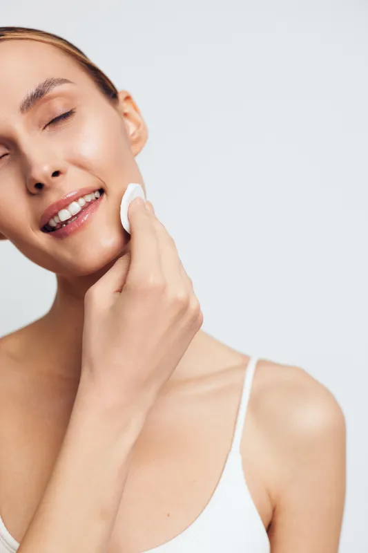 Woman closeup skincare beauty face, applying serum on cheek for hydration, spa treatment routine, natural smile, soft skin texture, gentle light, white background, calm copyspace