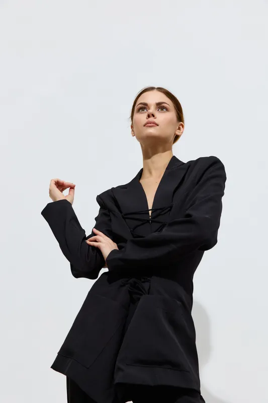 Fashion woman wearing black modern jacket poses against a plain light background with a confident and stylish expression, showcasing contemporary beauty and grace.