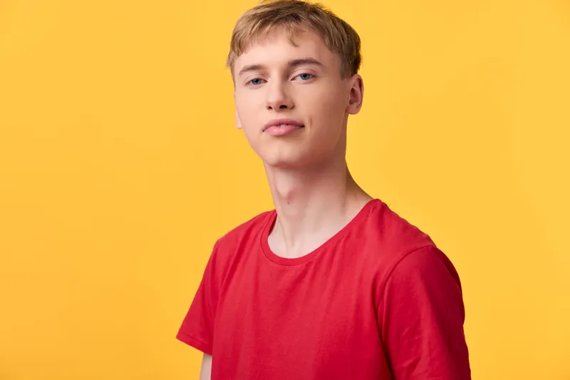 Youth man in casual red shirt stands against a bold yellow studio background, conveying relaxed fashion and contemporary style suitable for lifestyle, apparel, and stock photography
