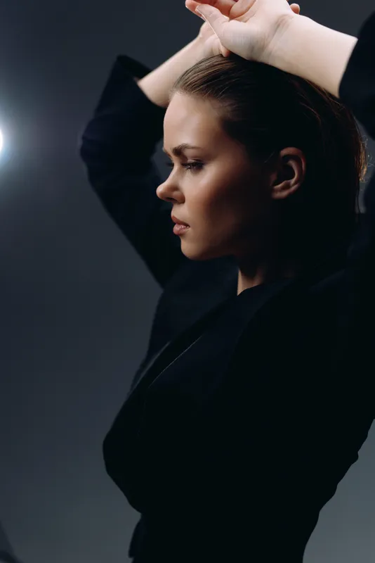 Profile of a thoughtful woman in black clothing with a dark studio background and soft lighting