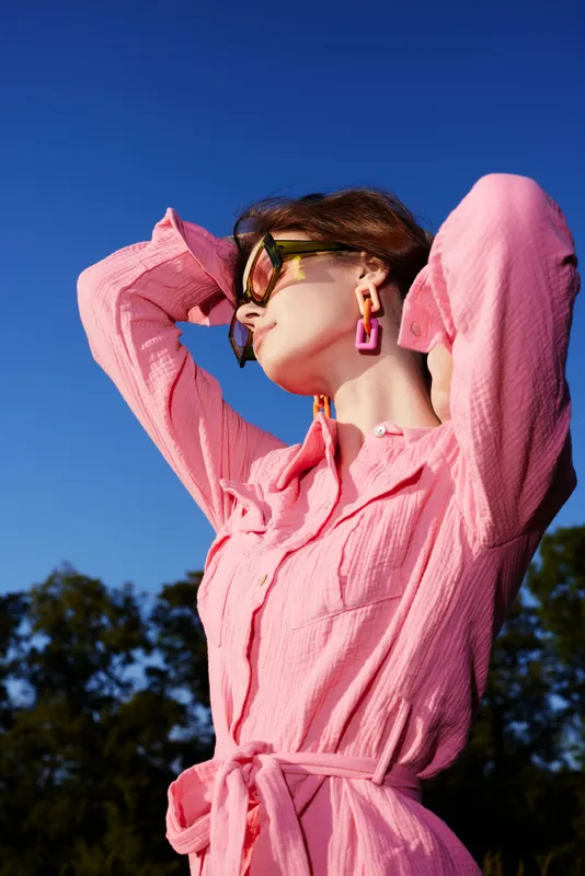 Elegant woman in a pink outfit enjoying a sunny day, showcasing confidence and style against a clear blue sky