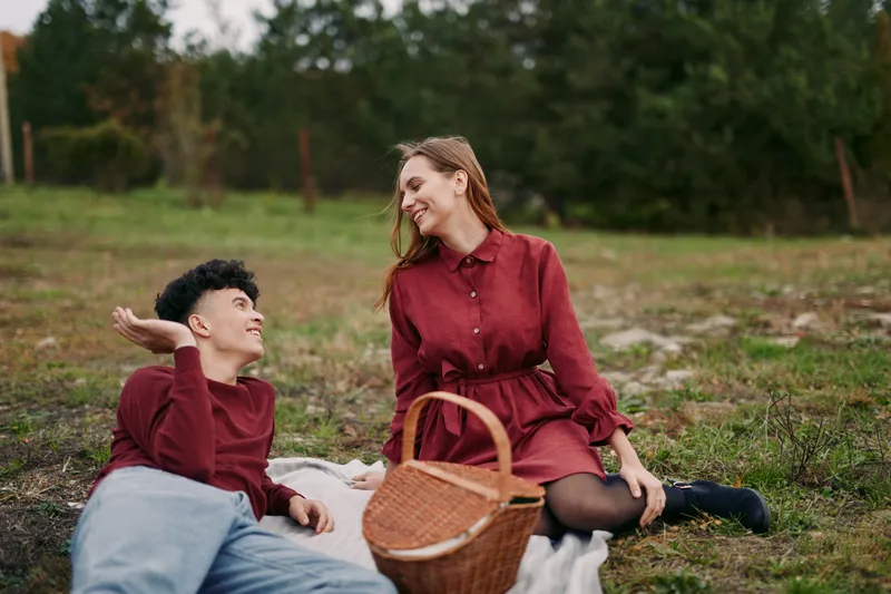 Young couple enjoying a relaxed outdoor picnic on a blanket, sharing candid smiles and gestures that convey an authentic and genuine connection in a natural, unstaged lifestyle moment.