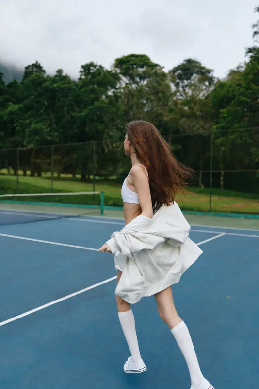 A young woman runs joyfully on a tennis court, wearing a stylish sports outfit, capturing the essence of active lifestyle and outdoor sports in a vibrant green background
