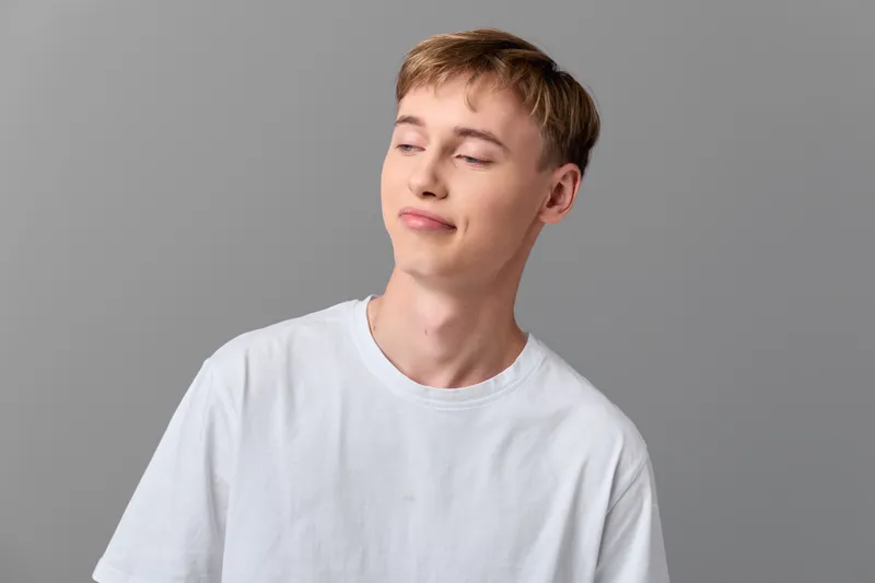 Young man in a white t shirt with a content smile in a relaxed studio setting, showcasing casual style, calm mood, and natural expressiveness.