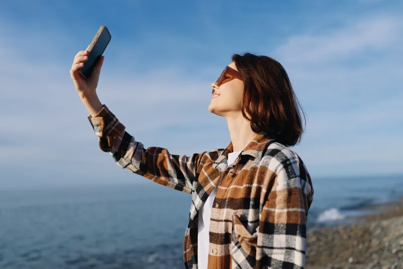 Selfie, woman, beach, portrait, smartphone, seaside, outdoors, sunny, casual, lifestyle photo of a woman posing with a phone by the water, capturing bright coastal mood and relaxed beach day
