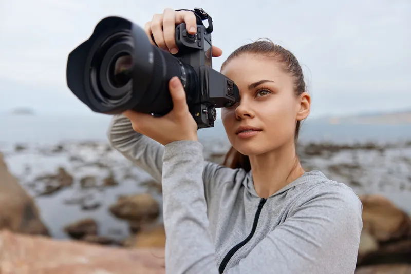 Young woman photographing landscape with a camera, showcasing her passion for photography by the seaside in a casual outfit