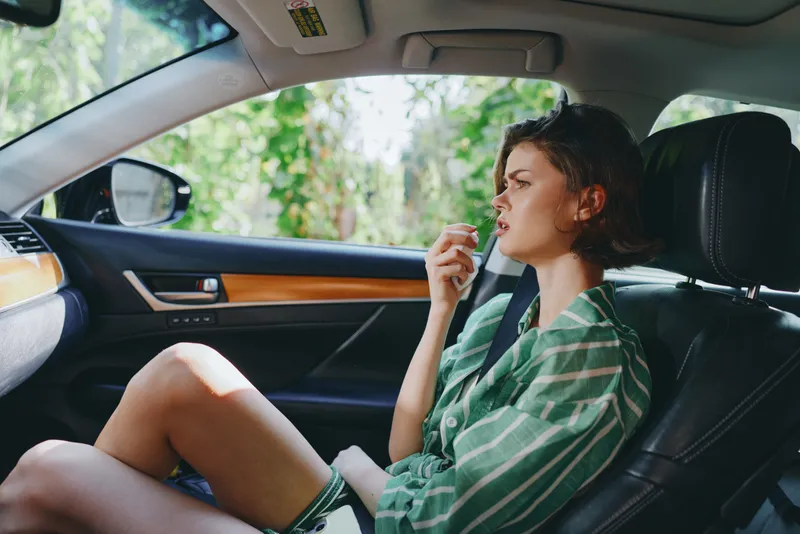 A woman sits in the front seat of a car, relaxed pose, green striped shirt, natural light highlighting her calm mood.