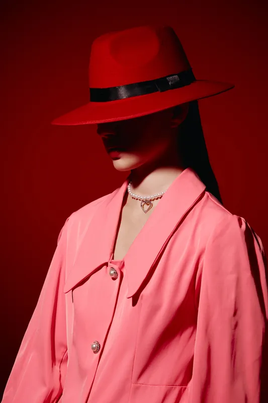 Fashion model wearing a wide brim red hat covering eyes and a pink coat in dramatic lighting studio shot. Concept of modern beauty, style, and creative fashion.
