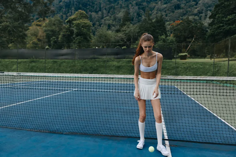 Athletic young woman preparing to serve a tennis ball on a sunny day at a green outdoor court, showcasing determination and focus in sportswear