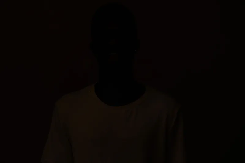 Portrait of an African male model in a casual white shirt, smiling against a dark background, reflecting joy and confidence, ideal for lifestyle and fashion concepts