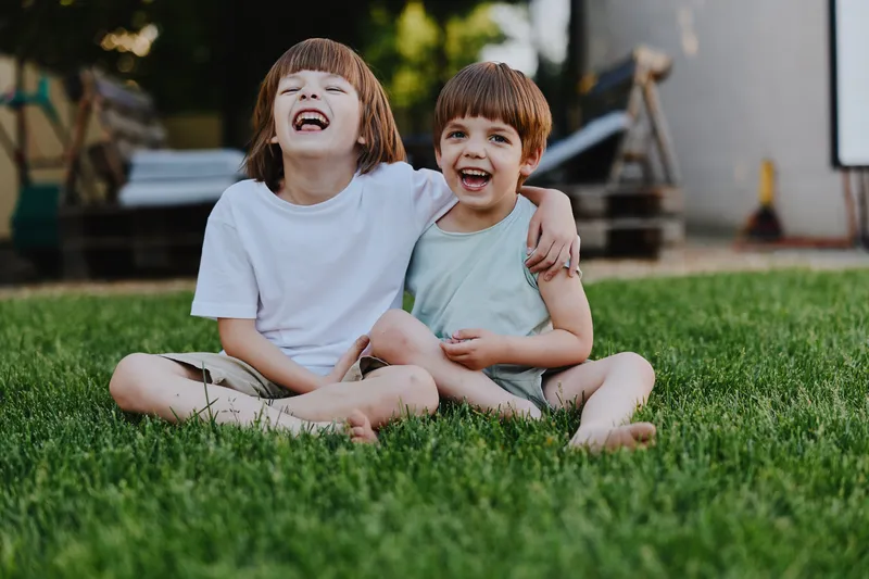 Two happy boys laughing together outdoors, enjoying a sunny day on the grass. Their carefree spirit and joy shine through in this vibrant moment.