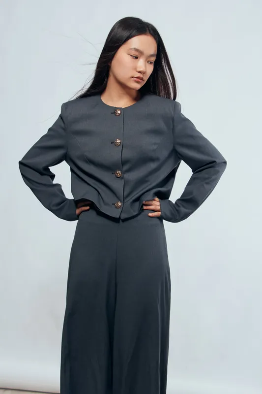 Young woman with long dark hair posing in modern dark gray outfit with buttoned jacket and matching skirt on light background. Fashion, style, elegance and confident model portrait.