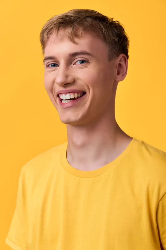 Man with a bright smile in a yellow tshirt stands in a studio with a bold background and warm lighting, delivering cheerful, friendly energy for lifestyle, fashion, and marketing visuals