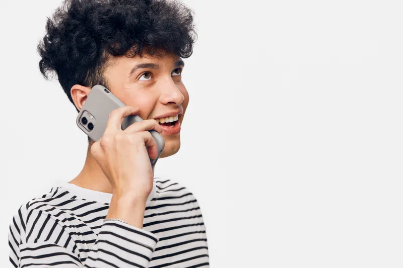 smiling man talking on smartphone, young adult with curly hair wearing striped shirt, expressive joyful facial expression, isolated white background