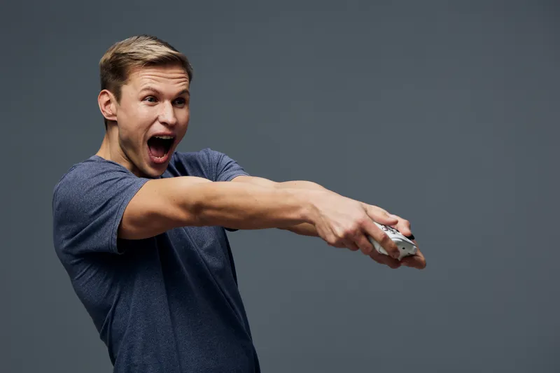 excited young caucasian man wear blue t-shirt hold remote control play video game isolated on gray background digital detox concept