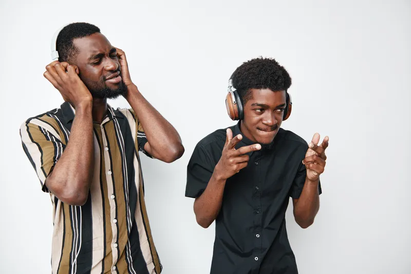 Two black men with dark skin wearing headphones enjoying music together in casual clothes on white background. Young African American friends having fun and dancing.