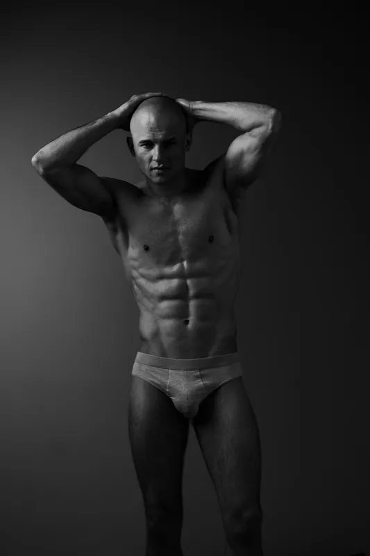 Athletic man showcasing a powerful physique in a stunning black and white portrait, emphasizing strength and confidence in a minimalist style.