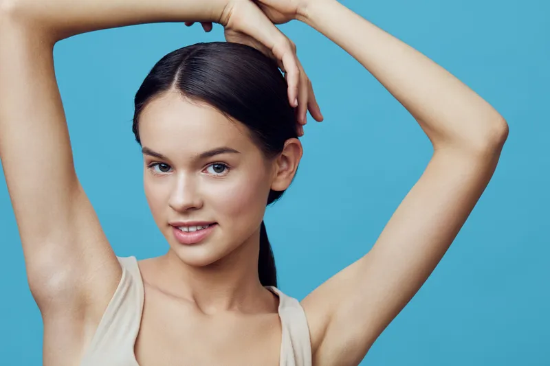 Smiling young woman with long dark hair and natural makeup, posing against a blue background with a light, fresh vibe Concept Beauty and self confidence