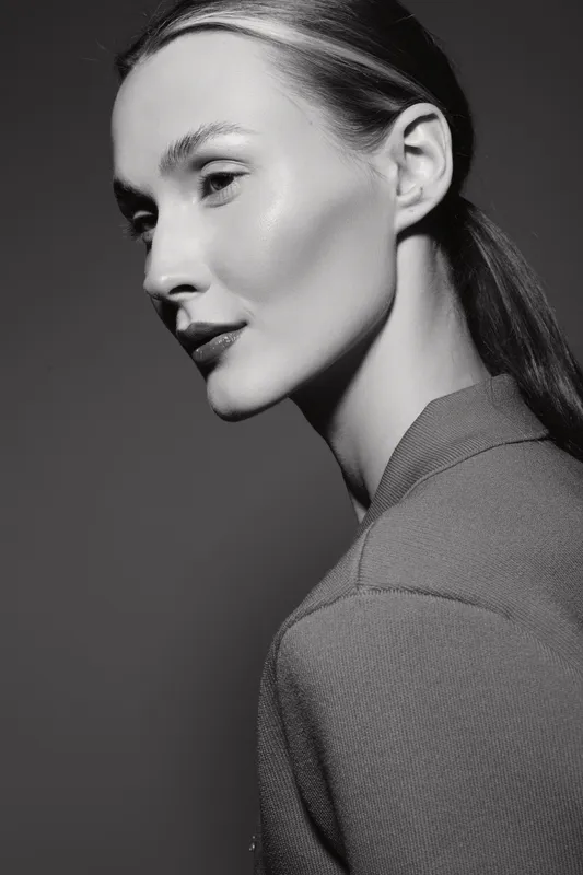 Portrait of a caucasian woman with light skin and slicked back hair wearing a high collar top, looking sideways in monochrome studio lighting. Concept of elegance and minimalism.
