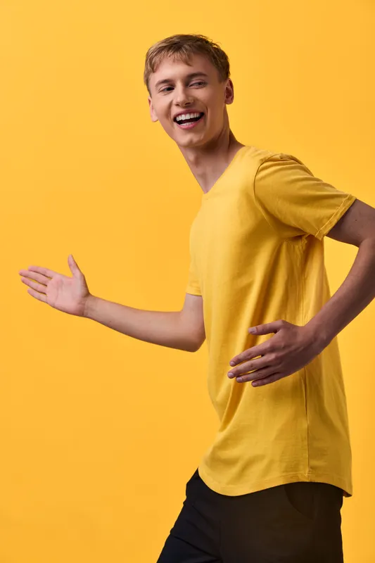 Cheerful man in a yellow shirt posing mid motion against a vibrant yellow backdrop, conveying energy, positivity, and dynamic casual style for lifestyle or fitness themes