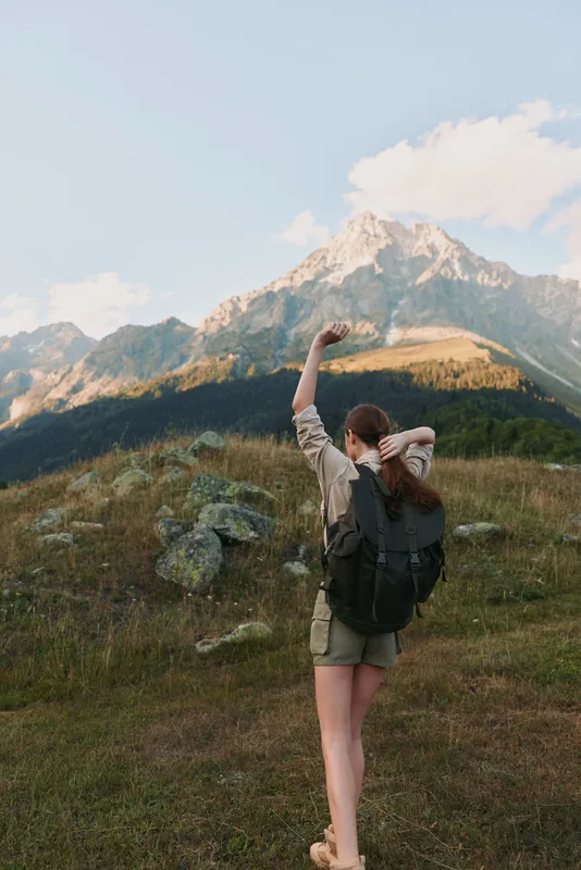 Woman hiker with backpack traverses a mountain trail, enjoying outdoors, expansive landscape, clear sky, sense of adventure and freedom in nature, travel lifestyle, photography moment