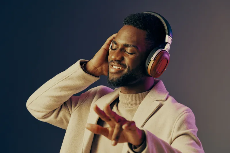 Smiling young Black man enjoying music with headphones, wearing a stylish cream coat against a gradient background Vibrant and soothing colors