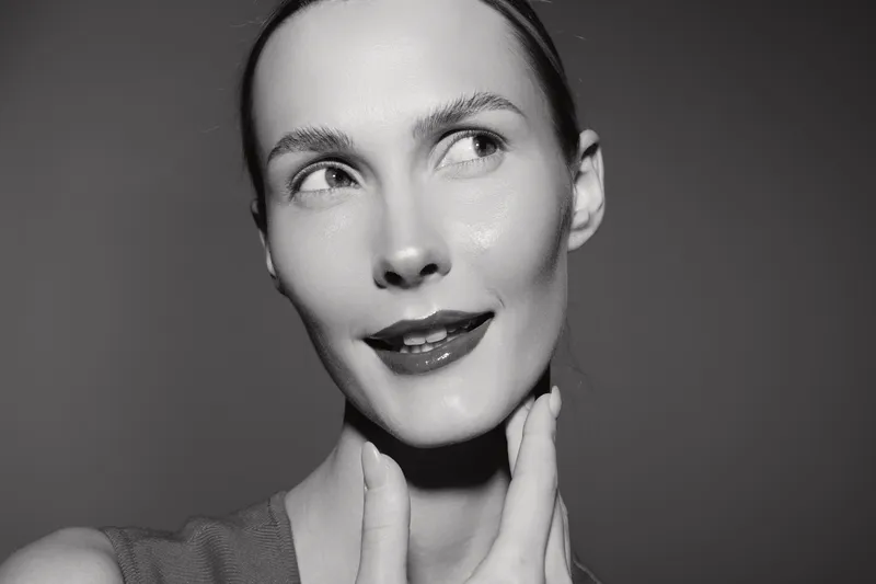 Portrait of a fair skinned caucasian woman with short hair smiling gently, touching her neck, studio lighting on grey background.