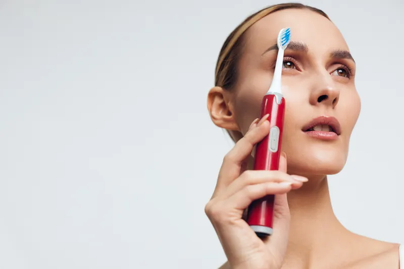 Close up of a woman brushing teeth with a red handle toothbrush, highlighting a smile and dental hygiene, illustrating oral care and self care in a fresh moment