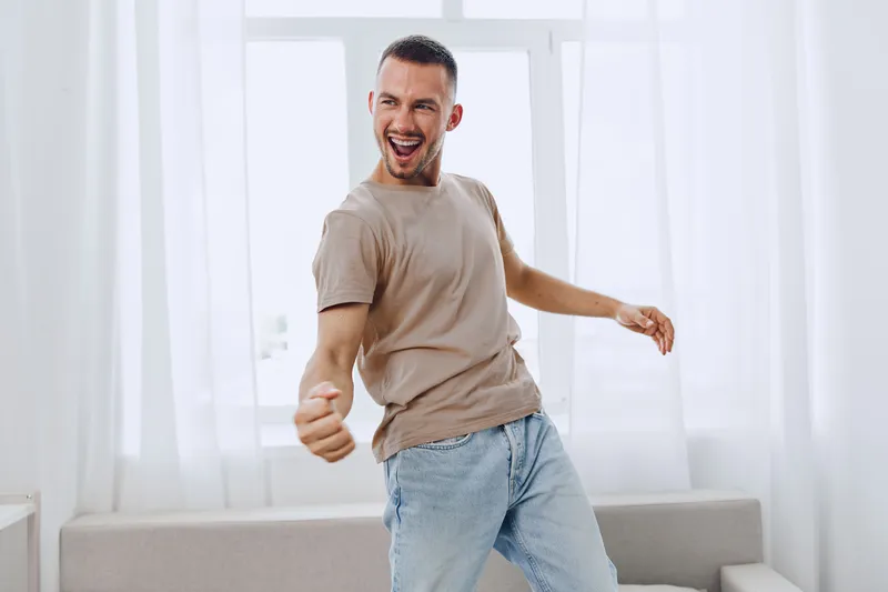Happy man dancing joyfully at home, embodying soft masculinity and emotional minimalism, enjoying a moment of self-expression and freedom from work pressures.