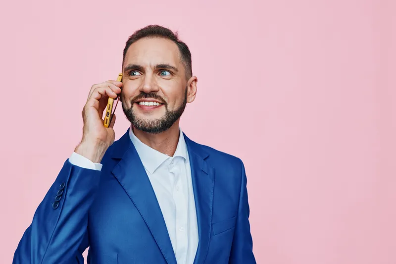 A business professional man stands against a vibrant colored background, smiling confidently while speaking on a mobile phone, conveying optimism and focus in a modern work scenario for creative