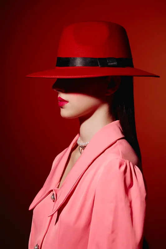Stylish woman in a red hat and pink coat poses sideways on red to black gradient background. Concept for fashion, beauty, and artistic editorial shoot with bold color contrast.