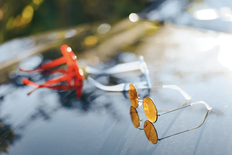 A close-up of sunglasses resting on a glossy surface under warm light, with a blurred natural background, evoking calm, style, and reflective mood that invites contemplation and storytelling.