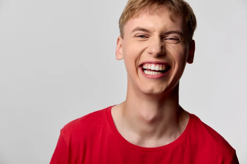 Smiling man in a red shirt grins with bright happiness and joyful energy, a candid studio closeup capturing cheerful mood and exuberant expression for upbeat, positive lifestyle and casual fashion