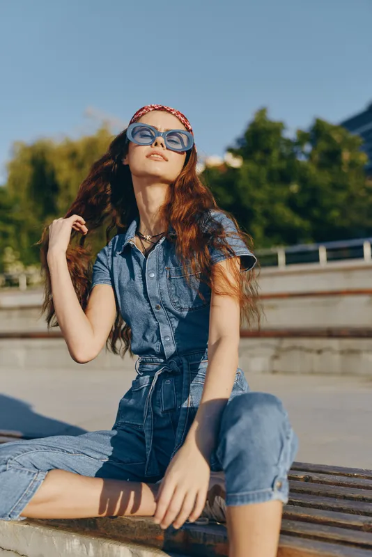 lifestyle woman in modern boho-western denim street style wearing sunglasses and a red bandana with film color effect under natural sunlight outdoors
