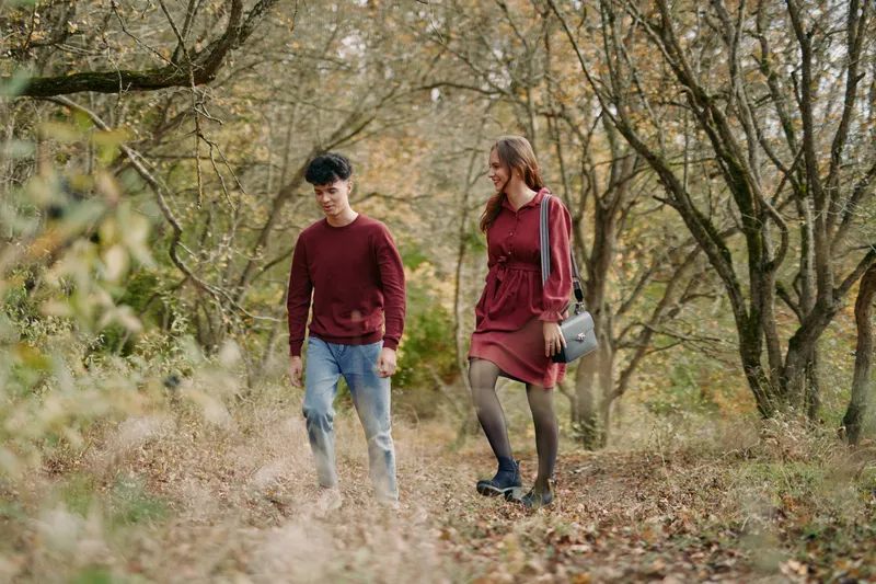 A candid autumn scene shows a young couple walking a woodland trail, emphasizing authenticity and natural connection with genuine expressions, warm light and credible everyday details.