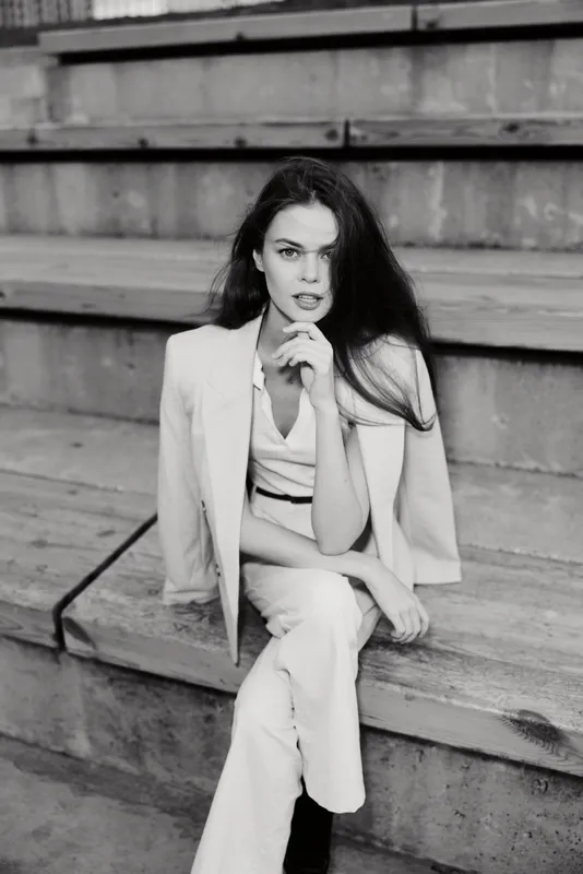 Woman in white business suit sitting on wooden stairs with confident expression black and white business fashion