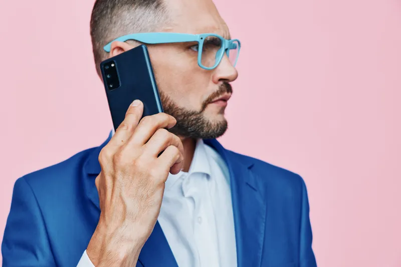 Professional man on an isolated colored background exudes confident, calm, and determined emotions while talking on a phone, portraying modern business communication and thoughtful mood in a