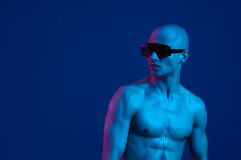 Athletic man wearing sunglasses, showcasing a striking contrast against a blue background, embodies modern style. This captivating image highlights strength and confidence.