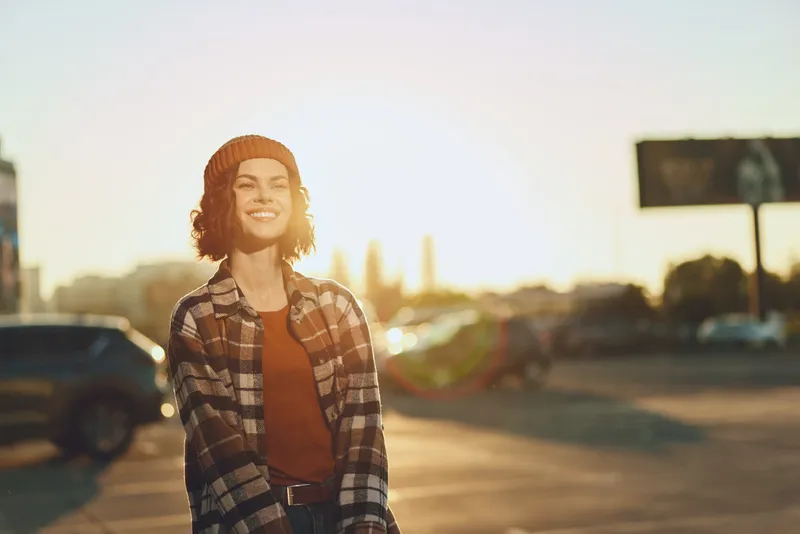 Woman smile in golden hour urban street, candid lifestyle portrait with beanie and flannel, authenticity and mindful living mood, warm golden hour glow and emotional storytelling.